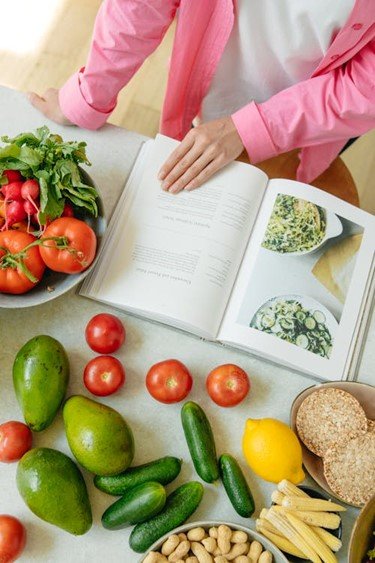 foto de uma mulher lendo um livro de receitas e cheio de legumes à volta